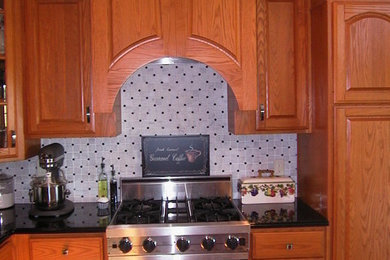 Example of a classic medium tone wood floor and brown floor kitchen design in Orange County with raised-panel cabinets, light wood cabinets, white backsplash, ceramic backsplash and stainless steel appliances