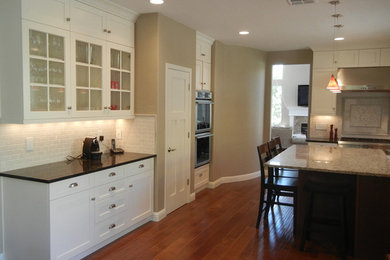 Example of a large transitional l-shaped medium tone wood floor kitchen pantry design in San Francisco with shaker cabinets, white cabinets, granite countertops, beige backsplash, ceramic backsplash, stainless steel appliances, an island and a farmhouse sink