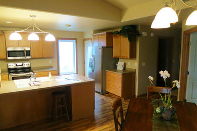 Photo of a medium sized traditional u-shaped kitchen/diner in Other with a built-in sink, flat-panel cabinets, light wood cabinets, stainless steel appliances, medium hardwood flooring, a breakfast bar and brown floors.