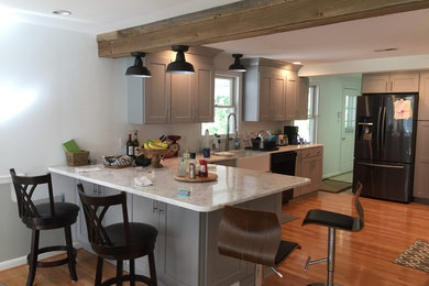 Inspiration for a mid-sized timeless l-shaped medium tone wood floor and brown floor open concept kitchen remodel in DC Metro with a farmhouse sink, raised-panel cabinets, gray cabinets, granite countertops, black appliances and a peninsula