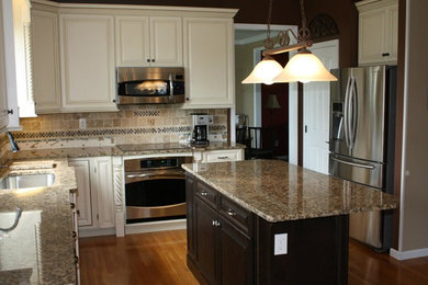 Example of a mid-sized l-shaped medium tone wood floor kitchen design in Cincinnati with a drop-in sink, raised-panel cabinets, beige cabinets, marble countertops, brown backsplash, mosaic tile backsplash, stainless steel appliances and an island