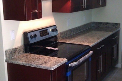 タンパにあるおしゃれなキッチン (落し込みパネル扉のキャビネット、赤いキャビネット、御影石カウンター、白いキッチンパネル、黒い調理設備、セラミックタイルの床) の写真