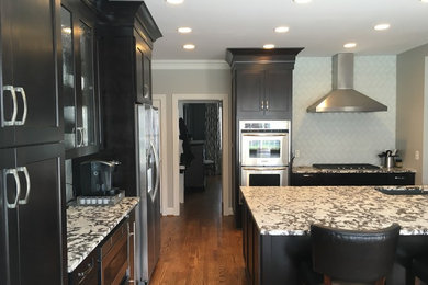 This is an example of a medium sized classic l-shaped kitchen/diner in Nashville with a submerged sink, shaker cabinets, black cabinets, white splashback, glass tiled splashback, stainless steel appliances, medium hardwood flooring, an island, brown floors and grey worktops.