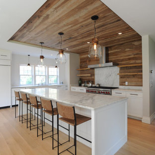 Mid-sized beach style l-shaped open plan kitchen in Boston with an undermount sink, shaker cabinets, white cabinets, marble benchtops, timber splashback, stainless steel appliances, light hardwood floors, with island and beige floor.