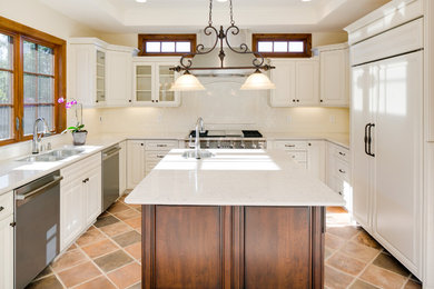 Example of a large tuscan u-shaped terra-cotta tile enclosed kitchen design in Los Angeles with a double-bowl sink, raised-panel cabinets, white cabinets, quartz countertops, white backsplash, ceramic backsplash, paneled appliances and an island
