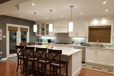 Example of a large transitional l-shaped dark wood floor and brown floor open concept kitchen design in Toronto with an undermount sink, shaker cabinets, white cabinets, quartz countertops, gray backsplash, subway tile backsplash, stainless steel appliances and an island