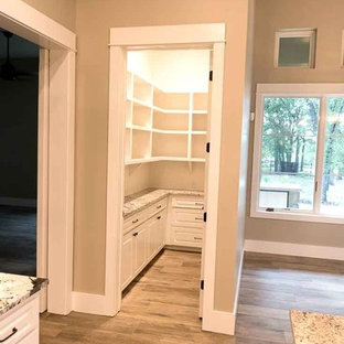 Mid-sized country u-shaped kitchen pantry in Austin with raised-panel cabinets, white cabinets, granite benchtops, medium hardwood floors, with island and beige floor.