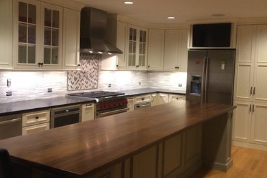 ボストンにある高級な中くらいなトラディショナルスタイルのおしゃれなキッチン (インセット扉のキャビネット、白いキャビネット、御影石カウンター、グレーのキッチンパネル、ボーダータイルのキッチンパネル、シルバーの調理設備、淡色無垢フローリング、茶色い床、黒いキッチンカウンター) の写真