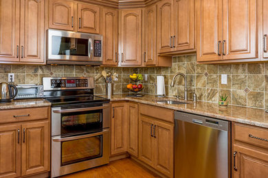 Inspiration for a mid-sized timeless l-shaped medium tone wood floor and brown floor enclosed kitchen remodel in Portland with an undermount sink, raised-panel cabinets, granite countertops, beige backsplash, porcelain backsplash, stainless steel appliances, no island and medium tone wood cabinets