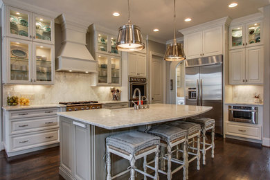 Open concept kitchen - large traditional l-shaped dark wood floor open concept kitchen idea in New Orleans with a farmhouse sink, raised-panel cabinets, white cabinets, marble countertops, white backsplash, stone slab backsplash, stainless steel appliances and an island