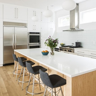 Idées déco pour une cuisine américaine scandinave en L de taille moyenne avec un placard à porte plane, un îlot central, un évier encastré, des portes de placard blanches, un plan de travail en quartz modifié, une crédence blanche, une crédence en carreau de verre, un électroménager en acier inoxydable et un sol en bois clair.