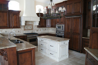 Mid-sized elegant u-shaped travertine floor and beige floor enclosed kitchen photo in Charlotte with a double-bowl sink, raised-panel cabinets, dark wood cabinets, granite countertops, beige backsplash, limestone backsplash, stainless steel appliances and an island