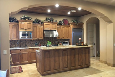 Inspiration for a mid-sized mediterranean l-shaped travertine floor and beige floor open concept kitchen remodel in Phoenix with an undermount sink, raised-panel cabinets, medium tone wood cabinets, granite countertops, multicolored backsplash, matchstick tile backsplash, stainless steel appliances and an island