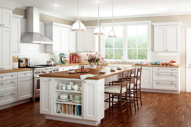 Inspiration for a large traditional l-shaped kitchen/diner in Tampa with a belfast sink, shaker cabinets, white cabinets, wood worktops, white splashback, metro tiled splashback, stainless steel appliances, medium hardwood flooring and an island.