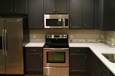 Mid-sized elegant u-shaped light wood floor and brown floor kitchen photo in Detroit with a double-bowl sink, shaker cabinets, black cabinets, solid surface countertops and stainless steel appliances