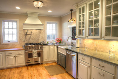 Inspiration for a mid-sized timeless l-shaped light wood floor and beige floor kitchen remodel in Oklahoma City with a farmhouse sink, glass-front cabinets, white cabinets, granite countertops, beige backsplash, ceramic backsplash and stainless steel appliances