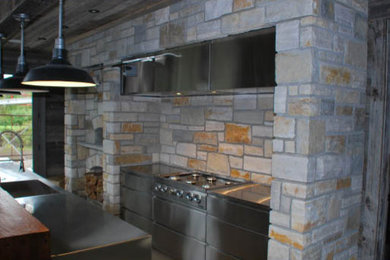 オタワにある広いおしゃれなキッチン (ドロップインシンク、フラットパネル扉のキャビネット、ステンレスキャビネット、ステンレスカウンター、マルチカラーのキッチンパネル、石タイルのキッチンパネル、シルバーの調理設備) の写真