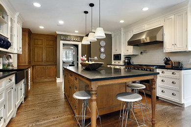 Example of a large classic medium tone wood floor eat-in kitchen design in New York with a farmhouse sink, white cabinets, white backsplash, subway tile backsplash, stainless steel appliances and an island