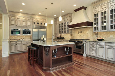 Inspiration for a large timeless l-shaped medium tone wood floor and brown floor enclosed kitchen remodel in Orlando with an undermount sink, glass-front cabinets, white cabinets, granite countertops, beige backsplash, ceramic backsplash, stainless steel appliances, an island and beige countertops