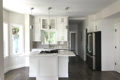 Inspiration for a mid-sized transitional l-shaped dark wood floor open concept kitchen remodel in Boston with an undermount sink, recessed-panel cabinets, white cabinets, solid surface countertops, gray backsplash, subway tile backsplash, stainless steel appliances and an island
