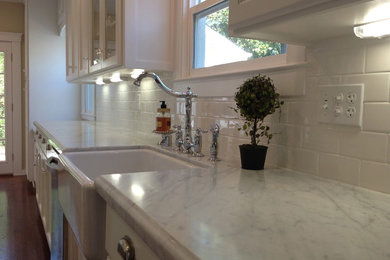 Photo of a large traditional single-wall enclosed kitchen in Sacramento with a belfast sink, recessed-panel cabinets, white cabinets, marble worktops, white splashback, metro tiled splashback, dark hardwood flooring, an island and brown floors.