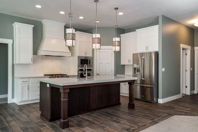 Inspiration for a mid-sized contemporary l-shaped dark wood floor and brown floor open concept kitchen remodel in Salt Lake City with a farmhouse sink, shaker cabinets, white cabinets, quartz countertops, white backsplash, glass tile backsplash, stainless steel appliances and an island