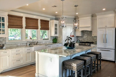 Example of a large transitional l-shaped medium tone wood floor and brown floor open concept kitchen design in Other with a farmhouse sink, recessed-panel cabinets, white cabinets, granite countertops, gray backsplash, stone tile backsplash, paneled appliances, an island and gray countertops