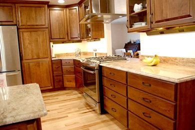 Geschlossene, Mittelgroße Klassische Küche in L-Form mit Doppelwaschbecken, profilierten Schrankfronten, hellbraunen Holzschränken, Granit-Arbeitsplatte, Küchengeräten aus Edelstahl, hellem Holzboden und Kücheninsel in Chicago