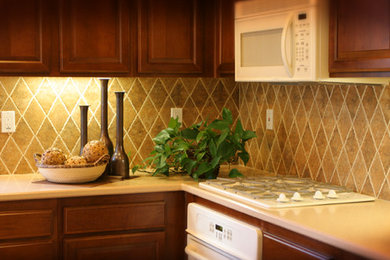 Example of a mid-sized classic l-shaped enclosed kitchen design in Albuquerque with raised-panel cabinets, medium tone wood cabinets, laminate countertops, beige backsplash, stone tile backsplash and white appliances