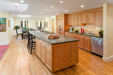 This is an example of a large traditional l-shaped kitchen/diner in Boston with an island, a single-bowl sink, shaker cabinets, light wood cabinets, composite countertops, beige splashback, integrated appliances, light hardwood flooring and brown floors.
