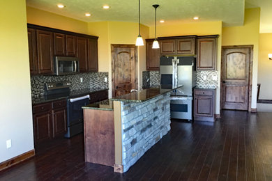 Example of a mid-sized classic dark wood floor and brown floor eat-in kitchen design in Other with an undermount sink, raised-panel cabinets, dark wood cabinets, granite countertops, multicolored backsplash, glass tile backsplash, stainless steel appliances and an island