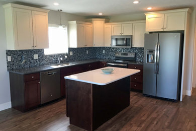 Mid-sized transitional l-shaped dark wood floor and brown floor kitchen photo in Other with an undermount sink, shaker cabinets, white cabinets, solid surface countertops, gray backsplash, glass tile backsplash, stainless steel appliances and an island