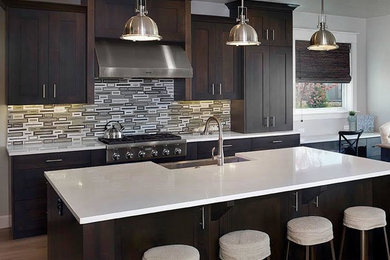 Eat-in kitchen - mid-sized contemporary l-shaped dark wood floor and brown floor eat-in kitchen idea in Philadelphia with a farmhouse sink, shaker cabinets, dark wood cabinets, solid surface countertops, multicolored backsplash, glass tile backsplash, stainless steel appliances and an island