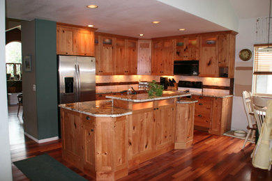 Example of a mid-sized mountain style l-shaped medium tone wood floor eat-in kitchen design in Denver with raised-panel cabinets, medium tone wood cabinets, granite countertops, ceramic backsplash, stainless steel appliances and an island