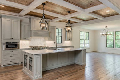 This is an example of a large classic l-shaped open plan kitchen in Phoenix with a submerged sink, beaded cabinets, grey cabinets, engineered stone countertops, white splashback, marble splashback, stainless steel appliances, medium hardwood flooring, an island, brown floors and white worktops.