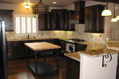 Example of a mid-sized classic u-shaped dark wood floor and brown floor enclosed kitchen design in Oklahoma City with an undermount sink, shaker cabinets, dark wood cabinets, granite countertops, beige backsplash, stone tile backsplash, stainless steel appliances and an island