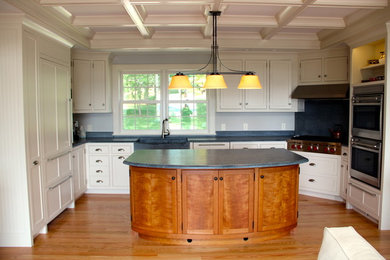 Enclosed kitchen - large traditional u-shaped light wood floor and brown floor enclosed kitchen idea in Other with white cabinets, an island, a farmhouse sink, shaker cabinets, soapstone countertops, black backsplash, stone slab backsplash, stainless steel appliances and black countertops