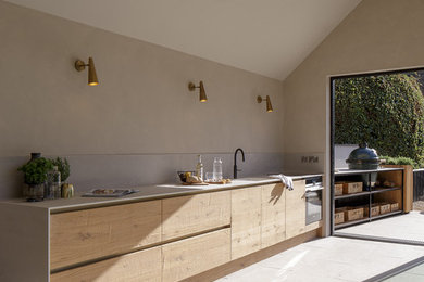 This is an example of a contemporary single-wall open plan kitchen in Other with an integrated sink, flat-panel cabinets, light wood cabinets, quartz worktops, white splashback, porcelain splashback, black appliances, no island and white worktops.