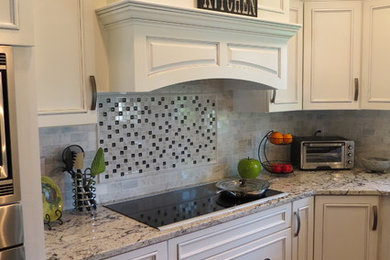 Large transitional l-shaped medium tone wood floor eat-in kitchen photo in New York with an undermount sink, recessed-panel cabinets, white cabinets, granite countertops, white backsplash, ceramic backsplash, stainless steel appliances and an island