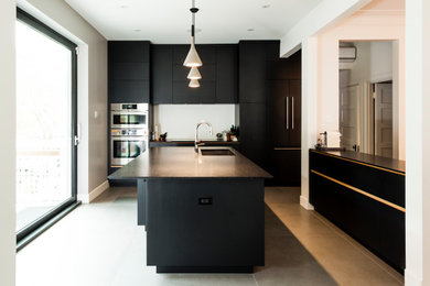 Example of a ceramic tile and gray floor kitchen design in Montreal with black cabinets, stainless steel appliances and black countertops