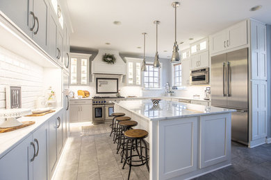 Example of a transitional gray floor kitchen design in DC Metro with an undermount sink, shaker cabinets, white cabinets, white backsplash, subway tile backsplash, stainless steel appliances, an island and white countertops