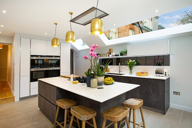 This is an example of a contemporary open plan kitchen in London with a submerged sink, flat-panel cabinets, black cabinets, white splashback, black appliances, an island, beige floors and white worktops.
