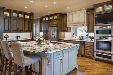 Example of a large classic l-shaped light wood floor eat-in kitchen design in Kansas City with an undermount sink, raised-panel cabinets, medium tone wood cabinets, granite countertops, ceramic backsplash, stainless steel appliances and an island