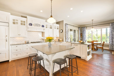 Inspiration for a mid-sized transitional l-shaped medium tone wood floor eat-in kitchen remodel in Indianapolis with a farmhouse sink, beaded inset cabinets, white cabinets, quartz countertops, white backsplash, subway tile backsplash, paneled appliances and an island
