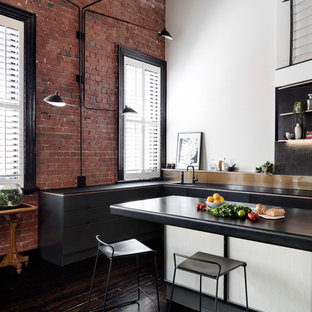 Photo of an industrial l-shaped kitchen in Melbourne with an undermount sink, flat-panel cabinets, black cabinets, black splashback, mosaic tile splashback, dark hardwood floors, with island, brown floor and black benchtop.