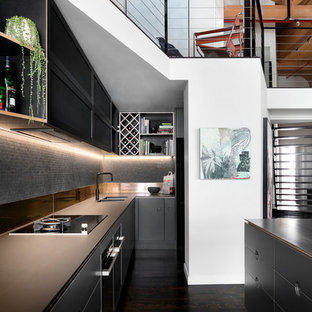 Inspiration for an industrial galley kitchen in Melbourne with an undermount sink, flat-panel cabinets, black cabinets, grey splashback, mosaic tile splashback, dark hardwood floors, with island, brown floor and brown benchtop.