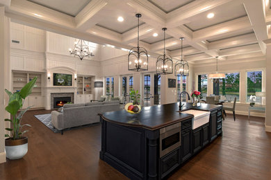 Foto de cocina clásica abierta con fregadero sobremueble, armarios con paneles con relieve, puertas de armario azules, electrodomésticos negros, suelo de madera en tonos medios, una isla, suelo marrón y encimeras marrones