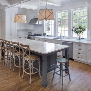 Diseño de cocina en L, clásica renovada, de tamaño medio, con fregadero bajoencimera, armarios estilo shaker, puertas de armario blancas, salpicadero blanco, electrodomésticos de acero inoxidable, suelo de madera en tonos medios, suelo marrón, encimera de mármol, salpicadero de azulejos de cerámica y una isla
