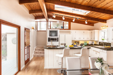 サンディエゴにある中くらいなトランジショナルスタイルのおしゃれなキッチン (フラットパネル扉のキャビネット、白いキャビネット、白い調理設備、淡色無垢フローリング) の写真