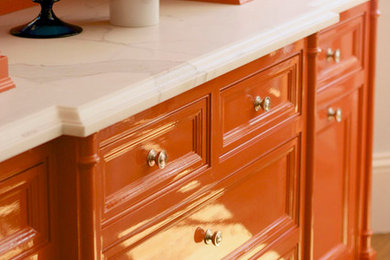 Exemple d'une cuisine américaine chic avec des portes de placard oranges et plan de travail en marbre.